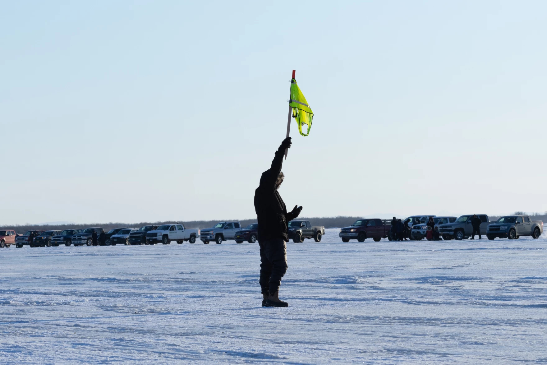 Kuskokwim 300 Race Manager Paul Basile raises the flag that will signify the mass start of the Akiak Dash. | Image: Josiah Swope, Article: Samantha Watson, KYUK